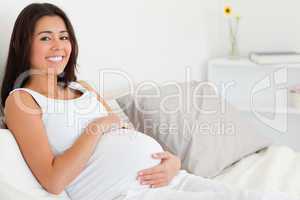 Cute pregnant woman touching her belly while lying on a bed