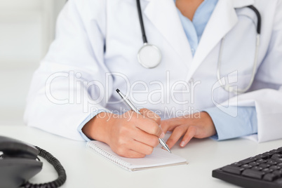 Female doctor with a stethoscope writing on a scratchpad