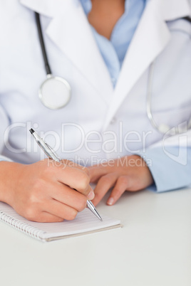 Young female doctor with a stethoscope writing on a scratchpad