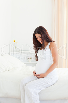 Good looking pregnant woman touching her belly while sitting on