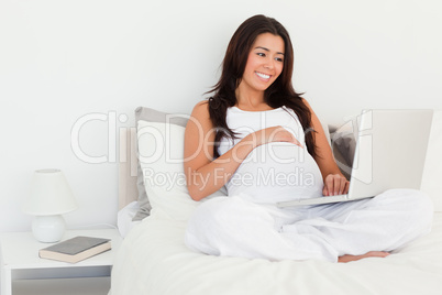 Beautiful pregnant woman relaxing with her laptop while lying on