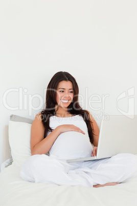 Attractive pregnant woman relaxing with her laptop while lying o