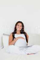 Good looking pregnant woman relaxing with her laptop while lying