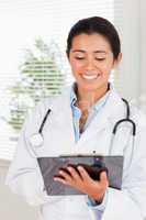 Beautiful female doctor with a stethoscope writing on a notebook