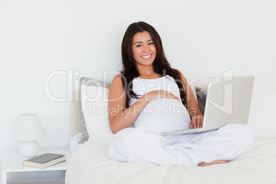 Pretty pregnant woman relaxing with her laptop while lying on a