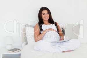 Pretty pregnant woman relaxing with her laptop while lying on a