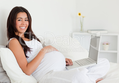 Charming pregnant woman relaxing with her laptop while lying on