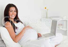 Charming pregnant woman relaxing with her laptop while lying on