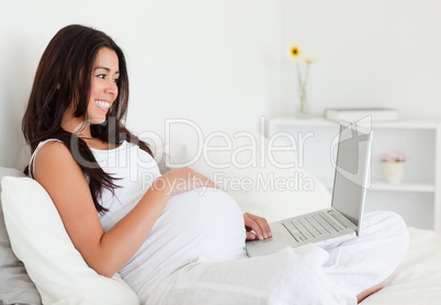 Lovely pregnant woman relaxing with her laptop while lying on a