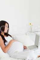 Gorgeous pregnant woman relaxing with her laptop while lying on