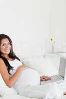 Cute pregnant woman relaxing with her laptop while lying on a be