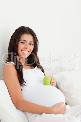 Gorgeous pregnant woman holding an apple on her belly while lyin