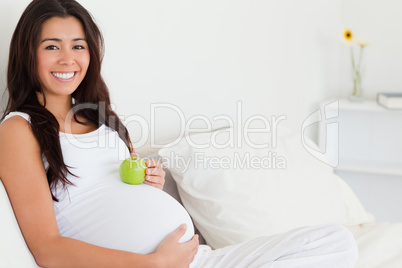 Beautiful pregnant woman holding an apple on her belly while lyi