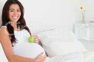 Beautiful pregnant woman holding an apple on her belly while lyi