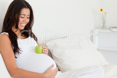 Attractive pregnant woman holding an apple on her belly while ly