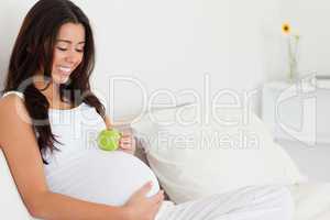 Attractive pregnant woman holding an apple on her belly while ly
