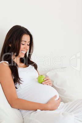 Good looking pregnant woman holding an apple on her belly while