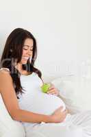 Good looking pregnant woman holding an apple on her belly while