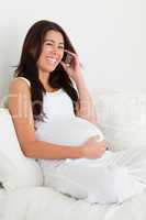 Beautiful pregnant woman on the phone while lying on a bed