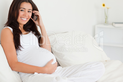 Pretty pregnant woman on the phone while lying on a bed