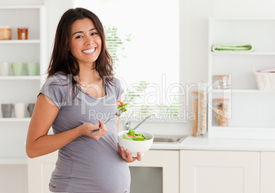 Attractive pregnant woman holding a bowl of salad while standing