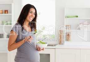 Beautiful pregnant woman holding a bowl of salad while standing