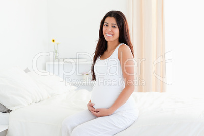 Beautiful pregnant woman touching her belly while sitting on a b