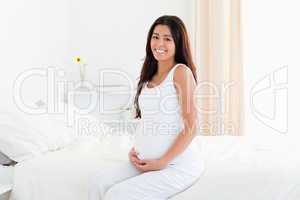 Beautiful pregnant woman touching her belly while sitting on a b