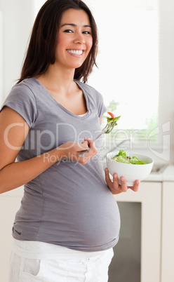 Pretty pregnant woman holding a bowl of salad while standing