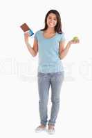 Pretty female holding a chocolate bar and an apple