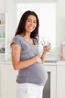 Pretty pregnant woman holding a glass of water while standing