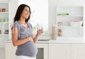 Gorgeous pregnant woman holding a glass of water while standing