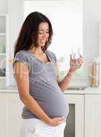 Charming pregnant woman holding a glass of water while standing