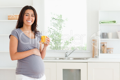 Charming pregnant woman holding a glass of orange juice while st