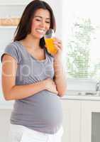 Attractive pregnant woman drinking a glass of orange juice while