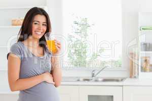 Beautiful pregnant woman drinking a glass of orange juice while