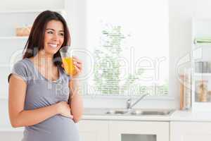 Good looking pregnant woman drinking a glass of orange juice whi