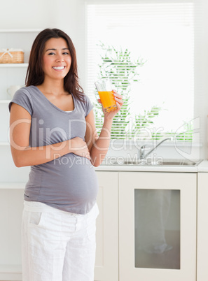 Gorgeous pregnant woman holding a glass of orange juice while st