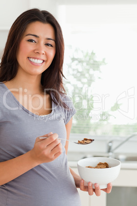 Gorgeous pregnant woman enjoying a bowl of cereals while standin