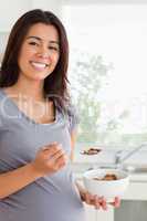 Gorgeous pregnant woman enjoying a bowl of cereals while standin