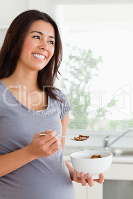 Attractive pregnant woman enjoying a bowl of cereals while stand