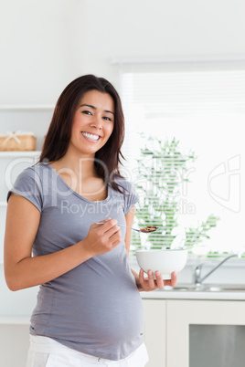 Good looking pregnant woman enjoying a bowl of cereals while sta