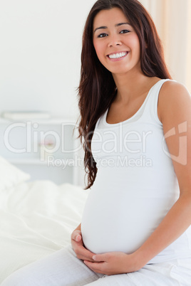 Portrait of a pretty pregnant woman touching her belly while sit