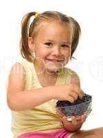 Cheerful little girl is eating blueberry