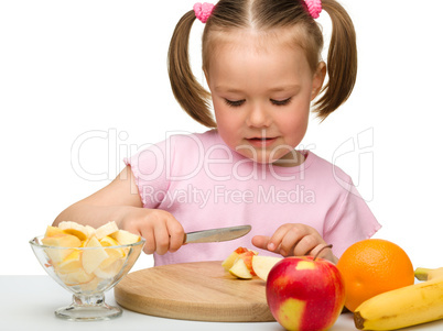 Little girl is cutting fruits for salad