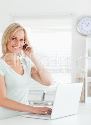 Blonde woman with a laptop and a phone looking into the camera