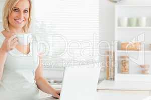 Smiling woman with a cup of coffee and a laptop looking into the