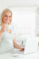 Charming woman with a cup of coffee and a laptop looking into th