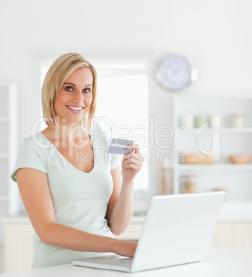 Blonde woman with credit card and notebook looks into camera