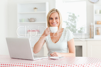 Woman drinking coffee with laptop in front of her looking into t Woman drinking coffee with laptop in front of her looking into t